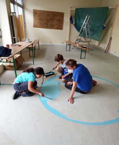 Bild von der Bauwoche: Kinder malen mit blauer Farbe einen Kreis auf den Boden.